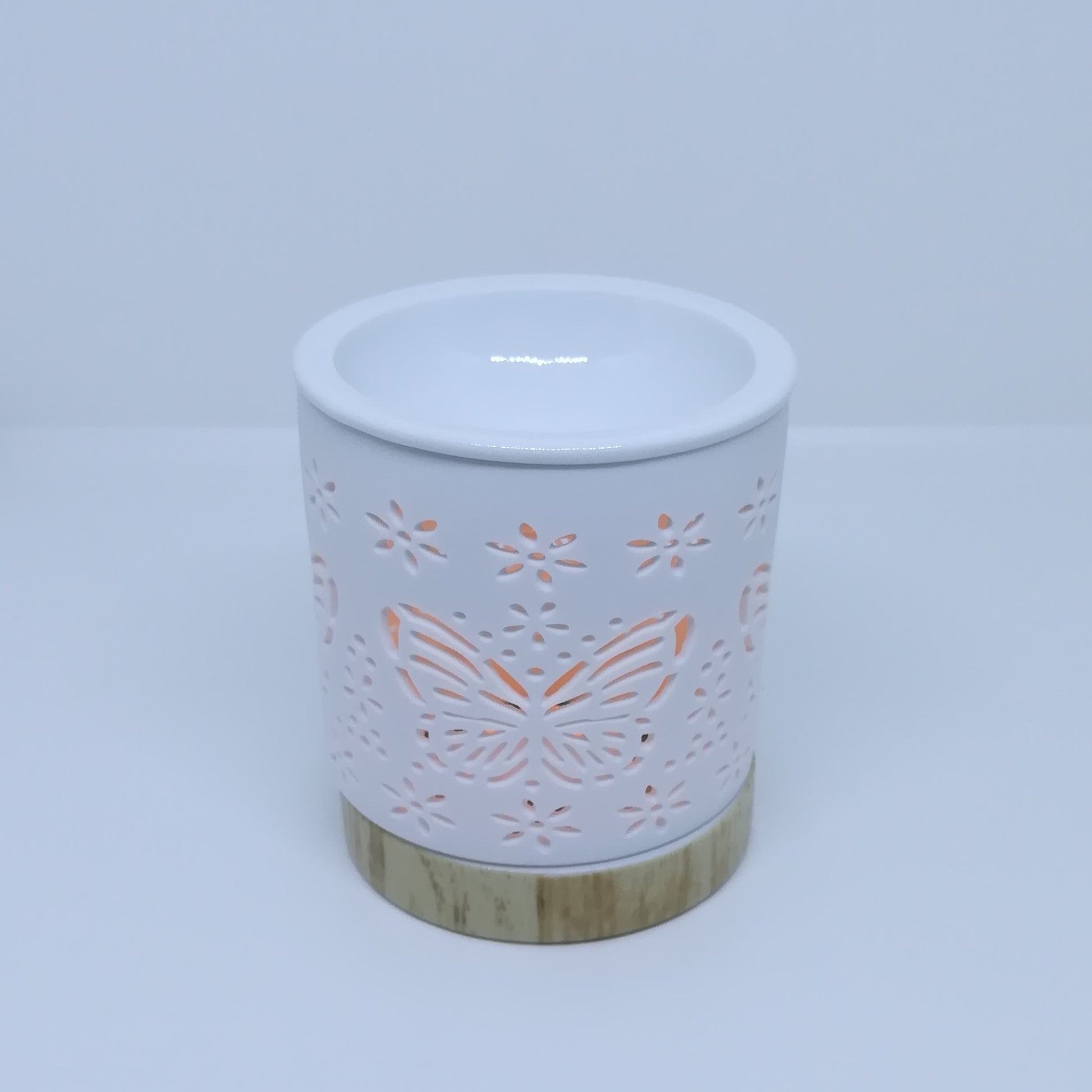 Ceramic white wax melt burner with ceramic wood effect base pictured under natural light with Butterfly apertures illuminated by the tealight within. (Tealight not included)