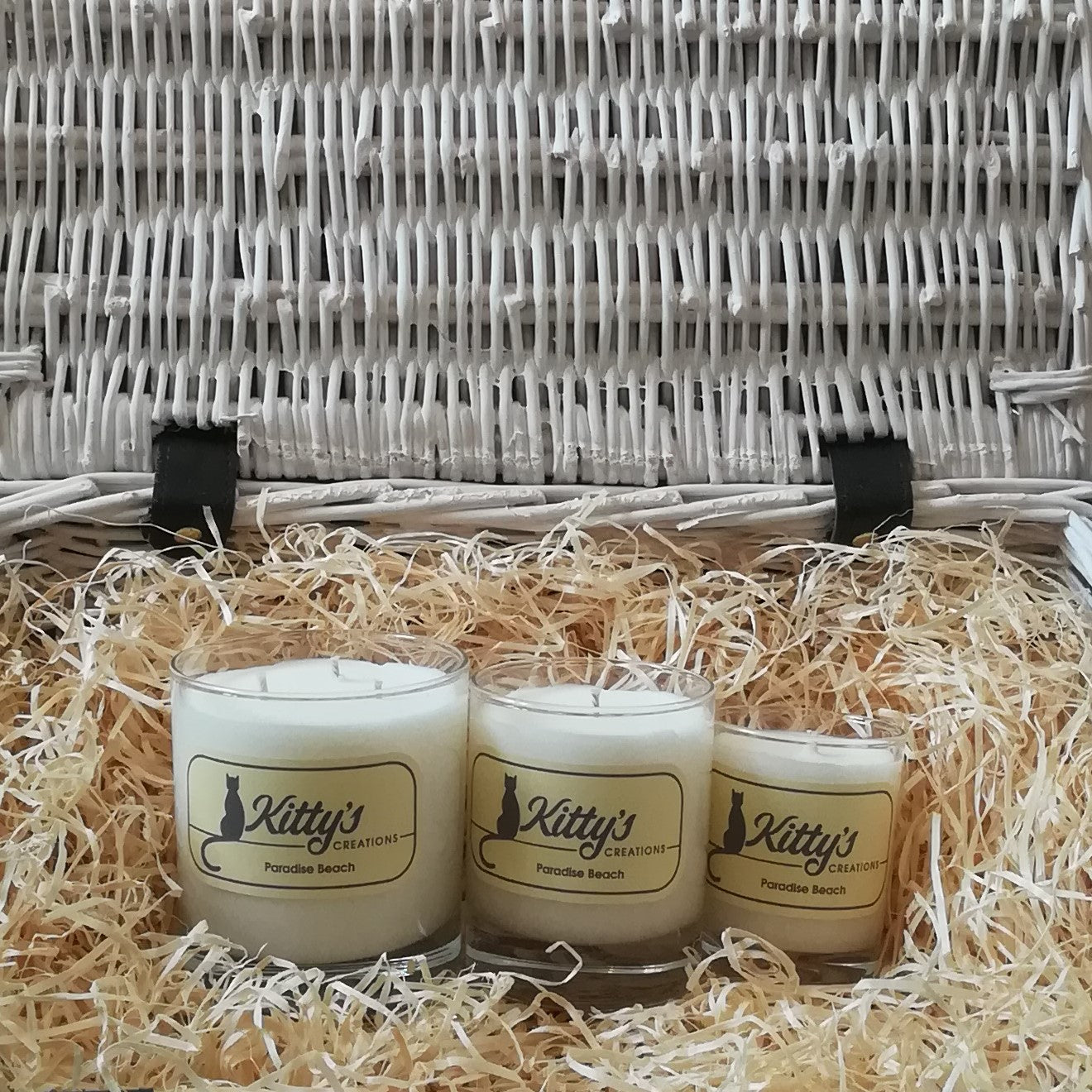 Three white candles, one large, one medium and one small are pictured in a basket of straw. Hand poured with soy wax, in elegant glass tumblers and available in three different sizes, these candles are the perfect gift. Each reveals a scent evoking warm sunshine, a tropical shore with pristine white sands, a perfect holiday.