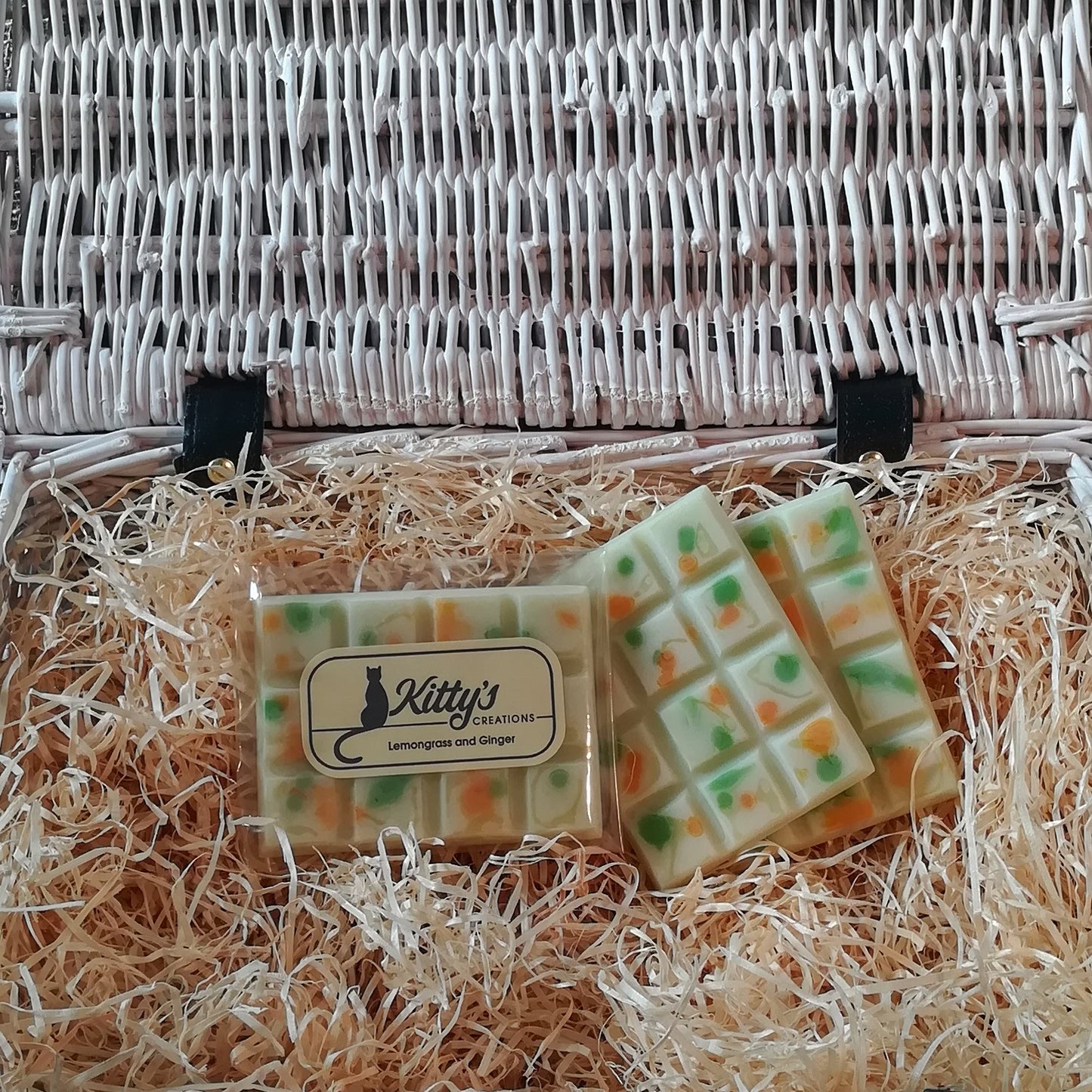 Three hand-made rectangular Wax Melts. Each is a light delicate green, overlaid with orange and forest green speckles and spots they are resting in a basket of straw. Each melt bursting with the mild and delicate fragrance of Lemongrass matched with the zesty freshness of ginger, combined to awaken your senses.