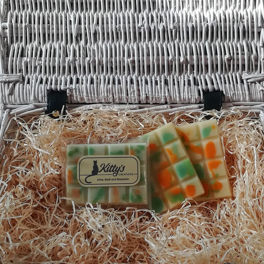 Three hand-made rectangular Wax Melts. Each is a light delicate green, overlaid with orange and fresh green speckles and spots they are resting in a basket of straw. Each melt containing mandarin and lime blend perfectly together before you sense the warmth of peppery basil and undertones of amberwood and caraway seeds taking you away on a tropical dream. 