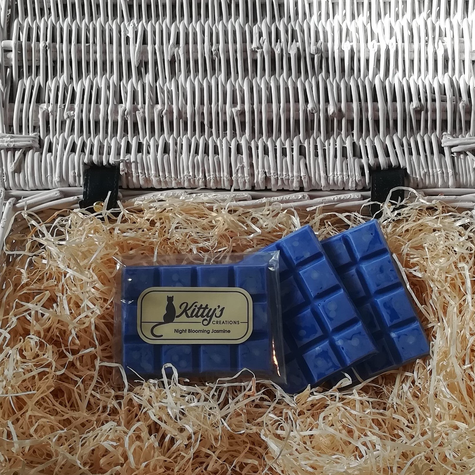 Three hand-made rectangular Wax Melts, each one midnight blue with a soft dusty surface and delicate Jasmine flowers beneath, resting in a basket of straw. Each melt reveals a delicate soothing Jasmine scent.