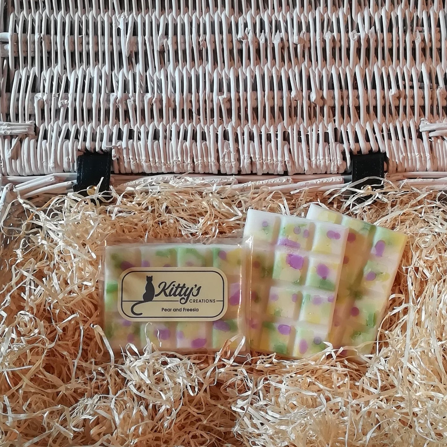 Three hand-made rectangular Wax Melts. Each is a natural wax cream colour, overlaid with fresh pear green, light yellow and purple speckles and resting in a basket of straw. Each melt bursting with the delicious aroma of fruity Pear entwining with the freshness of Freesia, combining to awaken and invigorate your senses.