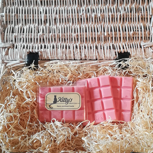 Three hand-made rectangular Wax Melts. Each is Geraldine pink resting in a basket of straw. Each melt effortlessly releases the subtle aroma of Peony mingled with the woody richness of Suede, filling your home with the essence of summer.